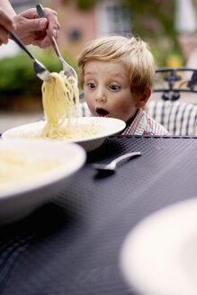 Boy sitting at garden table being served spaghetti, looking surprised - ISF11928