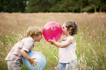Brother and sister in tall grass face to face playing with balloon - ISF11933