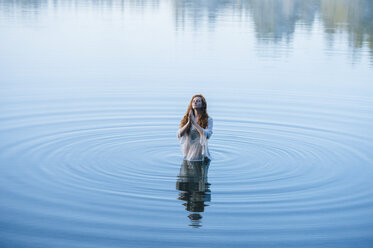 Young woman standing in lake ripples praying with eyes closed - ISF11942