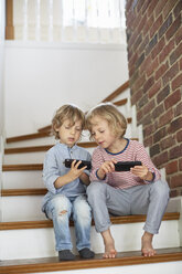 Zwei Jungen, die auf einer Treppe sitzen und auf ihre Smartphones schauen - ISF12053