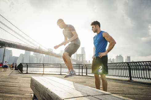 Personal trainer and young man training on riverside bench, Brooklyn, New York, USA - ISF12075