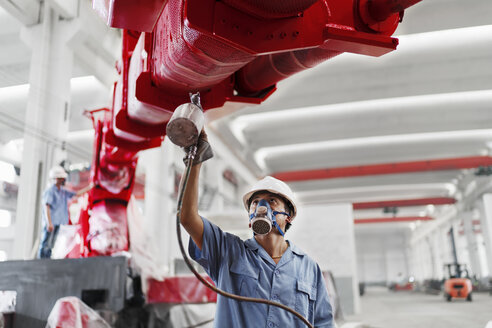 Männliche Arbeiter sprühen einen Kranarm in einer Fabrikhalle rot an, China - ISF12093