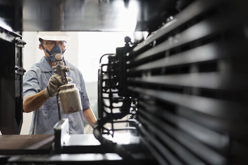 Männlicher Arbeiter, der in einer Spritzkabine einer Kranfabrik Bauteile schwarz lackiert, China - ISF12094