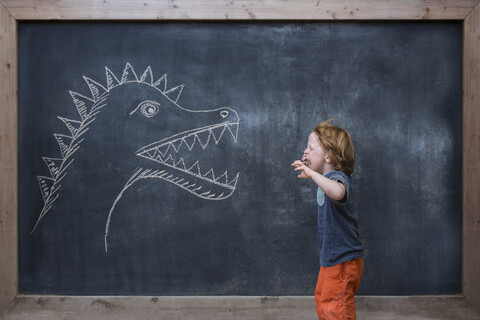 Junge brüllt Dinosaurierzeichnung an der Tafel an, lizenzfreies Stockfoto