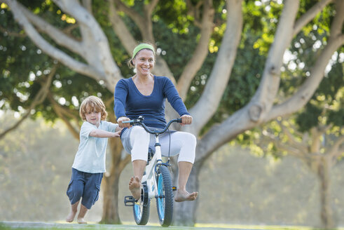 Mutter sitzt auf dem Fahrrad des Sohnes, der Sohn schiebt sie an - ISF12168