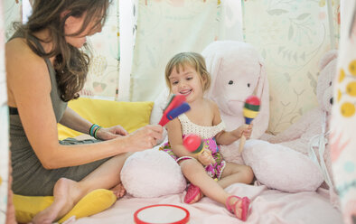 Mother and daughter sitting in play tent, playing with musical instruments - ISF12169