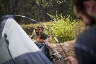 Young couple putting up tent on riverside, Lake Tahoe, Nevada, USA - ISF12235