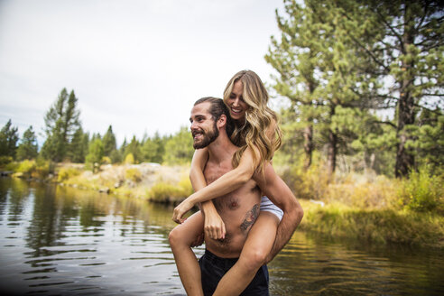 Young man giving girlfriend piggyback in river, Lake Tahoe, Nevada, USA - ISF12242