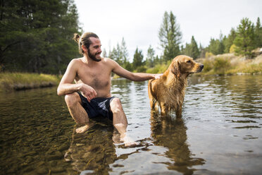 Junger Mann sitzt im Fluss und streichelt seinen Hund, Lake Tahoe, Nevada, USA - ISF12245