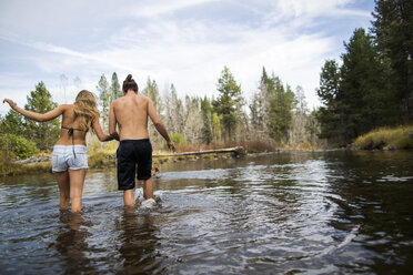Rear view of young couple crossing river, Lake Tahoe, Nevada, USA - ISF12246
