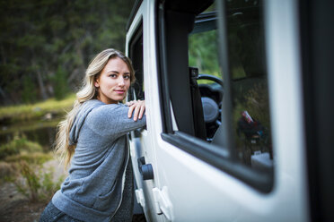 Portrait of young woman leaning against jeep at riverside, Lake Tahoe, Nevada, USA - ISF12259