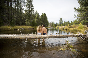Rear view of romantic young couple sitting on fallen tree in river, Lake Tahoe, Nevada, USA - ISF12268