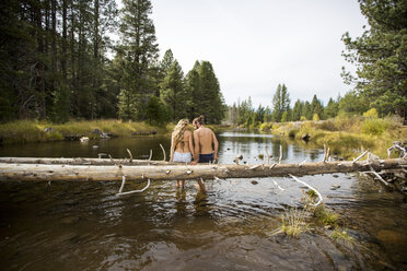 Rückansicht eines romantischen jungen Paares, das auf einem umgestürzten Baum im Fluss sitzt, Lake Tahoe, Nevada, USA - ISF12268