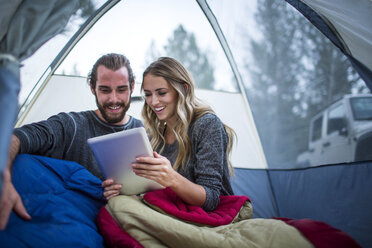 Young couple reading digital tablet in tent, Lake Tahoe, Nevada, USA - ISF12276