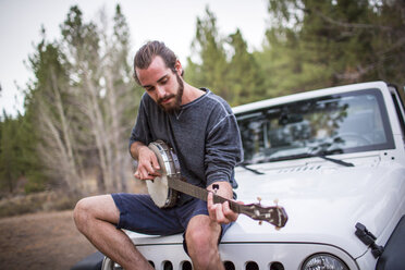 Junger Mann spielt Banjo auf der Motorhaube eines Jeeps, Lake Tahoe, Nevada, USA - ISF12277