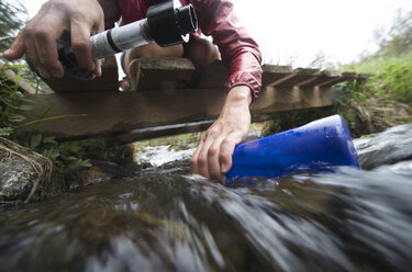 Oberflächenansicht einer Wanderin mit Wasserfilter, die ihre Wasserflasche im Bach füllt - ISF12350