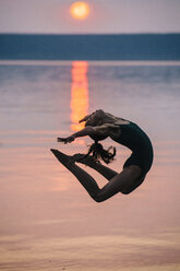 Side view of girl by ocean at sunset, leaping in mid air bending backwards - ISF12359