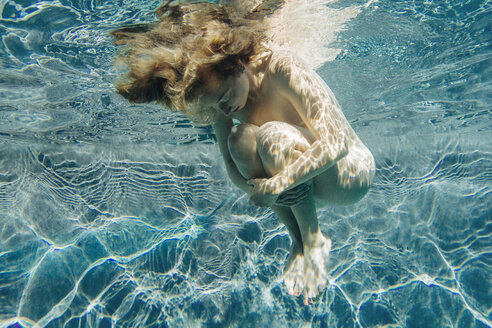 Low angle view of young woman in swimming pool, hugging knees, head down eyes closed - ISF12372