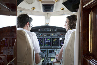 Rückansicht von männlichen und weiblichen Piloten, die sich im Cockpit eines Privatjets unterhalten - ISF12388