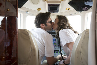 Rear view of male and female pilots kissing in cockpit of private jet - ISF12389