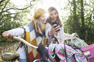 Teenager-Mädchen im Wald halten Fahrräder mit Smartphone zu nehmen selfie lächelnd - ISF12539