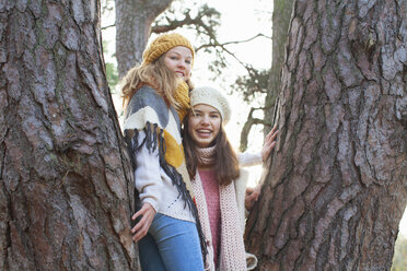 Portrait of teenage girls standing in tree looking at camera smiling - ISF12546