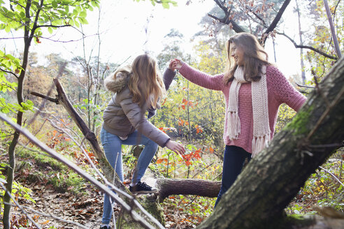 Teenager-Mädchen im Wald hilft einem Freund beim Klettern auf einen umgestürzten Baumstamm und lächelt - ISF12554