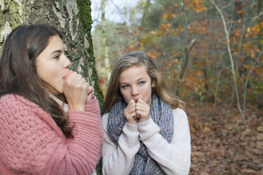 Teenage girls in forest hands over mouth mimicking animal noise, looking away - ISF12559