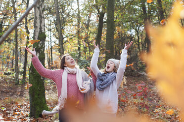 Teenage girls in forest arms raised throwing autumn leaves smiling - ISF12560