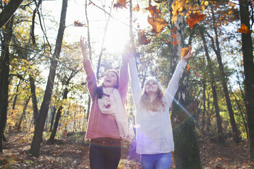 Teenage girls in forest arms raised throwing autumn leaves, looking up smiling - ISF12562