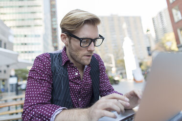 Gestresster junger Geschäftsmann, der in einem Straßencafé auf einem Laptop tippt, New York, USA - ISF12571