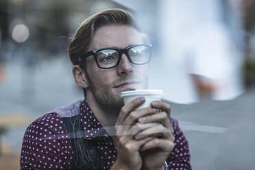 Trauriger junger Geschäftsmann hinter dem Schaufenster der Stadt, der Kaffee zum Mitnehmen trinkt - ISF12572