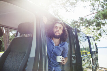 Young man having coffee in van by lake - ISF12594