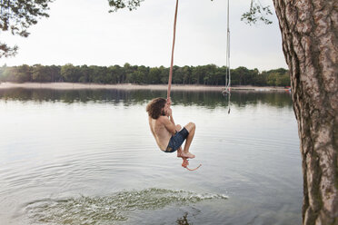 Young man rope swinging above lake stock photo