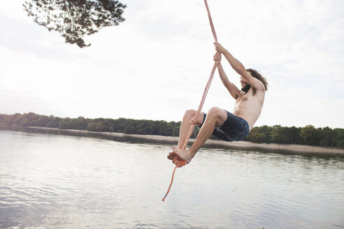 Young man rope swinging above lake - ISF12606