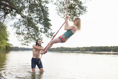 Young woman rope swinging above lake - ISF12610
