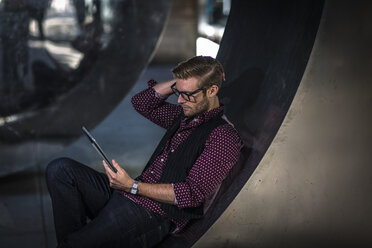 Junger Geschäftsmann, der an einer gebogenen Wand lehnt und ein digitales Tablet liest - ISF12638