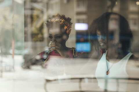 Porträt einer Frau hinter einer Fensterscheibe, die ein Glas Wasser trinkt, lizenzfreies Stockfoto