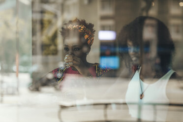 Porträt einer Frau hinter einer Fensterscheibe, die ein Glas Wasser trinkt - OCAF00316