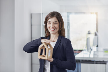 Porträt einer lächelnden jungen Geschäftsfrau, die ein Architekturmodell im Büro hält - RORF01259