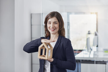 Portrait of smiling young businesswoman holding architectural model in office - RORF01259