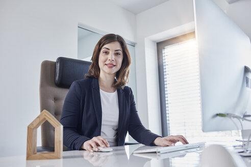 Porträt einer lächelnden jungen Geschäftsfrau am Schreibtisch im Büro mit einem Architekturmodell - RORF01260
