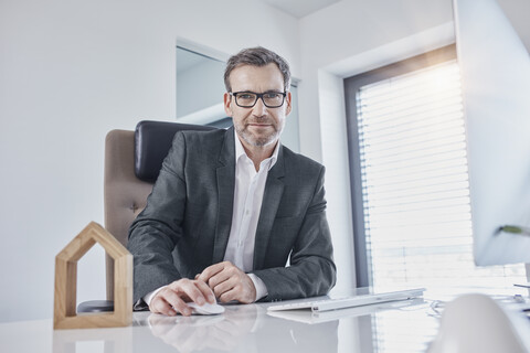 Porträt eines Geschäftsmannes am Schreibtisch im Büro mit Architekturmodell, lizenzfreies Stockfoto