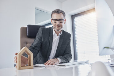 Portrait of businessman at desk in office with architectural model - RORF01266