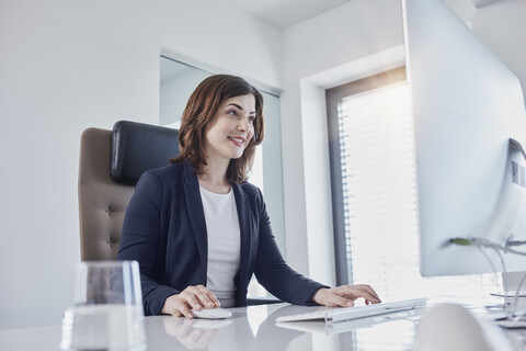 Lächelnde junge Geschäftsfrau bei der Arbeit am Schreibtisch im Büro, lizenzfreies Stockfoto