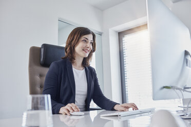 Smiling young businesswoman working at desk in office - RORF01270