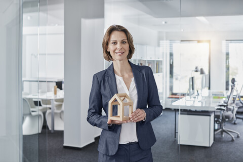 Porträt einer lächelnden Geschäftsfrau, die ein Architekturmodell im Büro hält, lizenzfreies Stockfoto