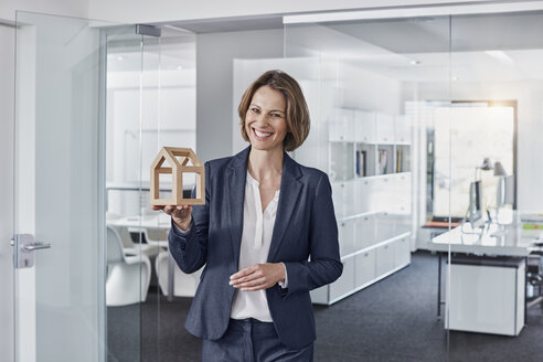 Porträt einer lächelnden Geschäftsfrau, die ein Architekturmodell im Büro hält - RORF01272