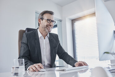 Glücklicher Geschäftsmann arbeitet am Schreibtisch im Büro - RORF01280