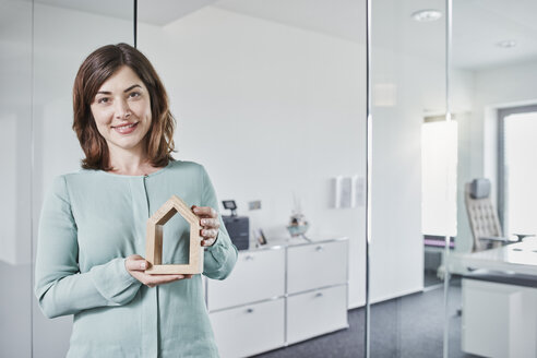 Porträt einer lächelnden jungen Geschäftsfrau, die ein Architekturmodell im Büro hält - RORF01283